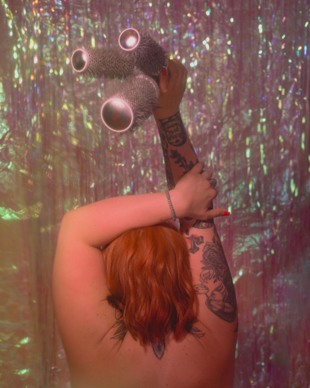 Tattooed woman with red hair holds a disco ball aloft against a holographic glitter backdrop.