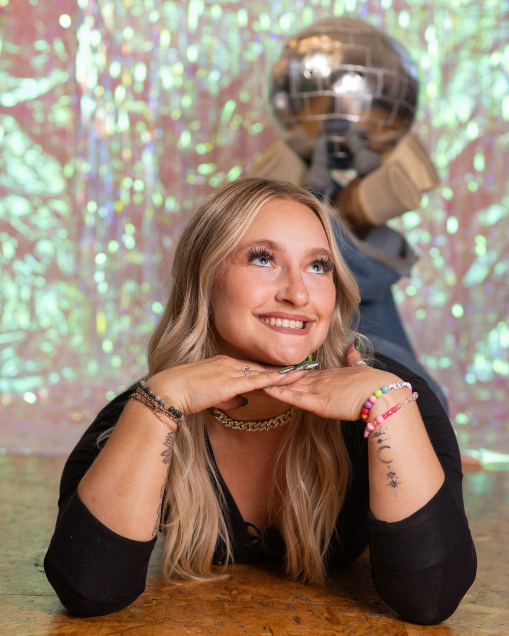 Smiling blonde woman poses with a disco ball in a holographic studio setting.