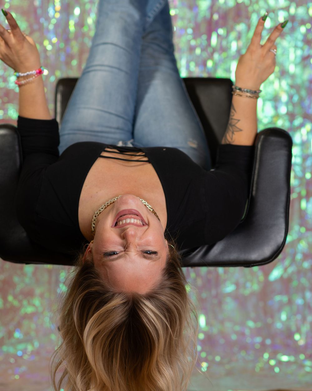 Blonde woman laughs upside down in a chair against a shimmering holographic backdrop.