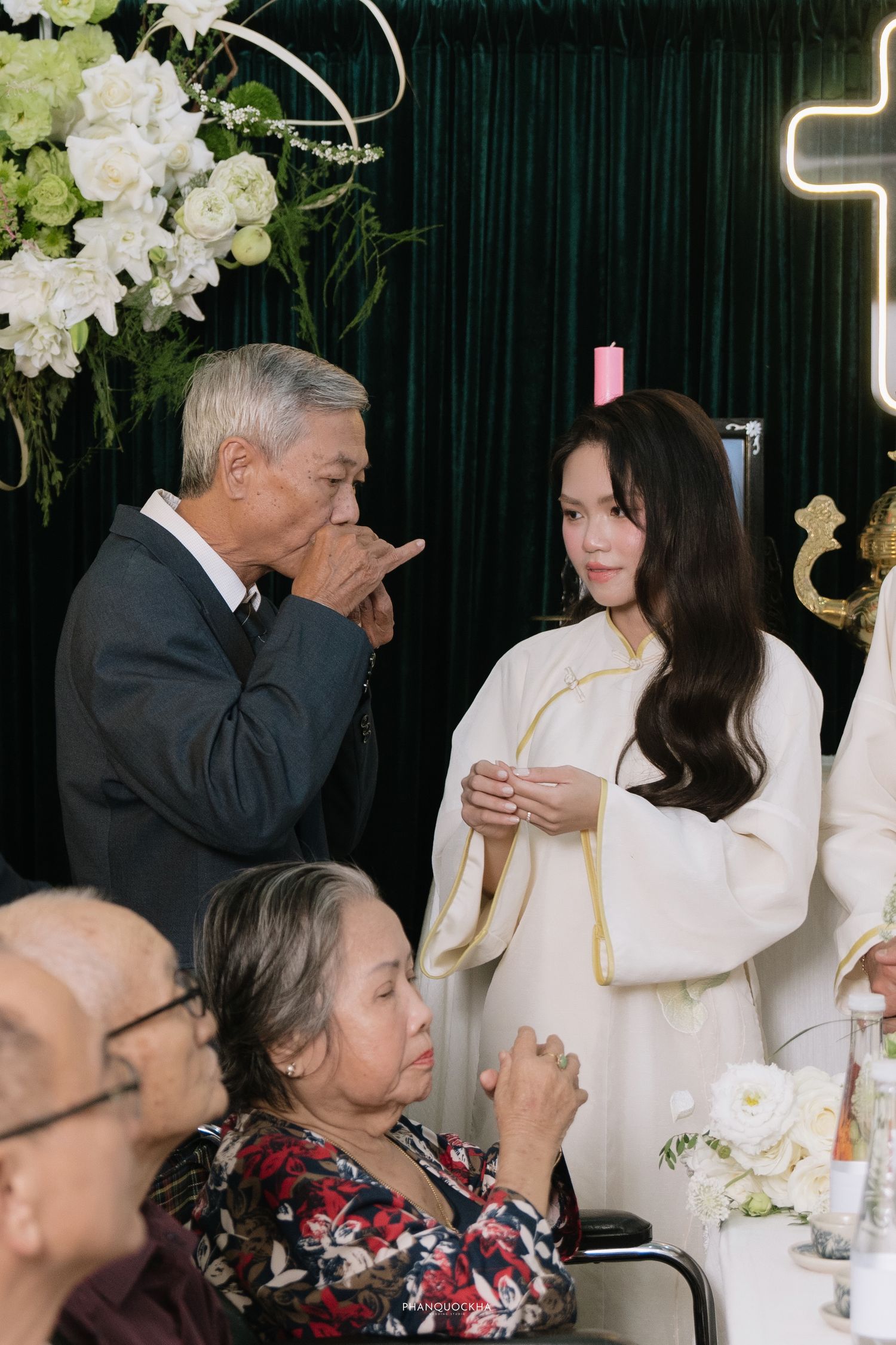 Older man gesturing while speaking to bride in white ao dai at traditional Vietnamese engagement ceremony.
