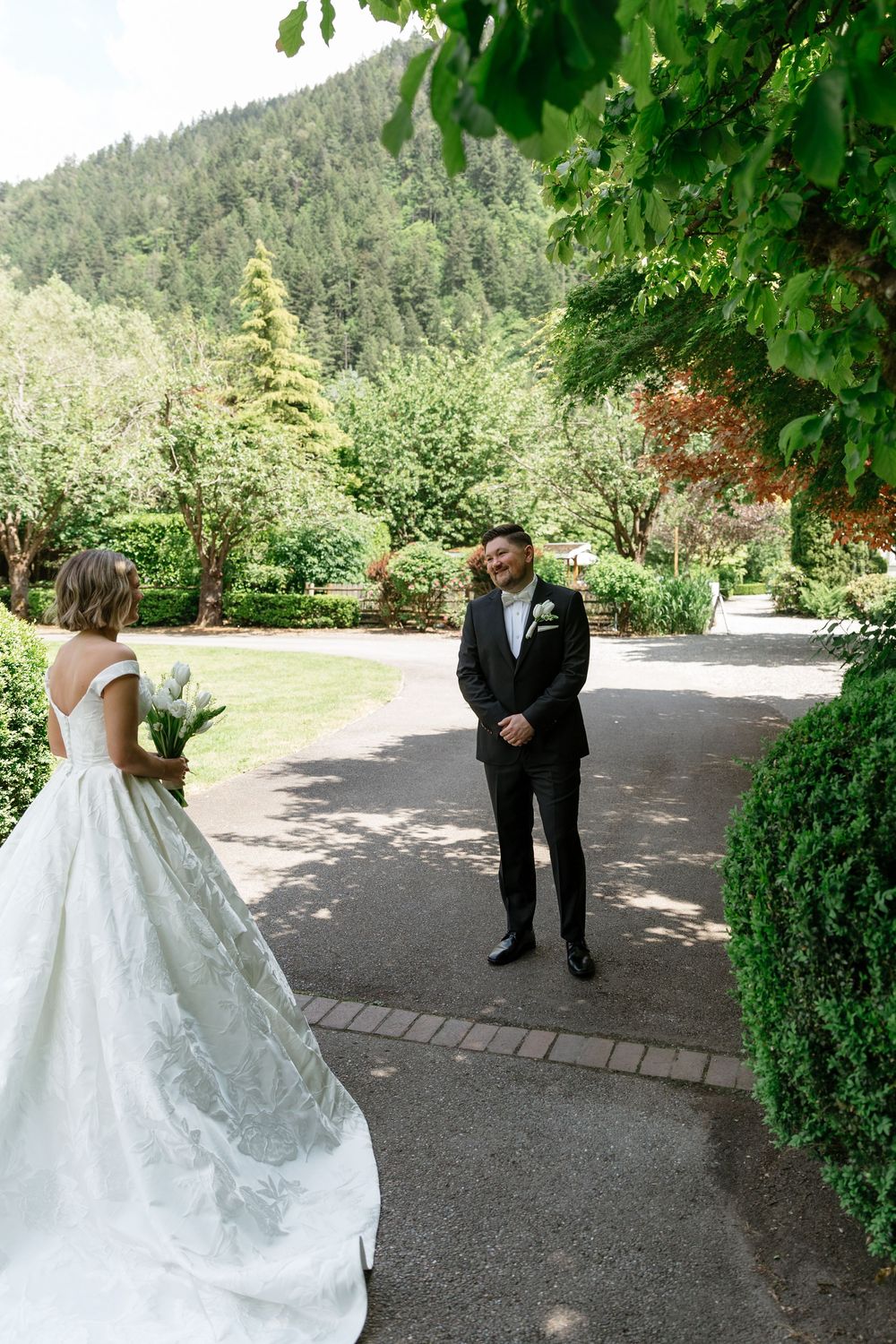A series of wedding first look photos showing a bride in a white gown surprising her groom in a garden setting.