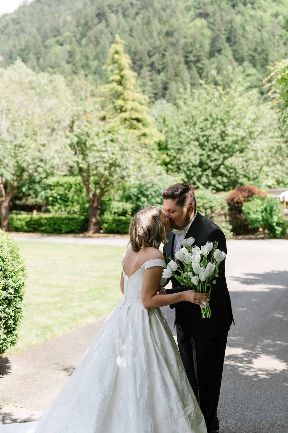 A couple shares their first look moment on a garden path surrounded by lush greenery and trees.