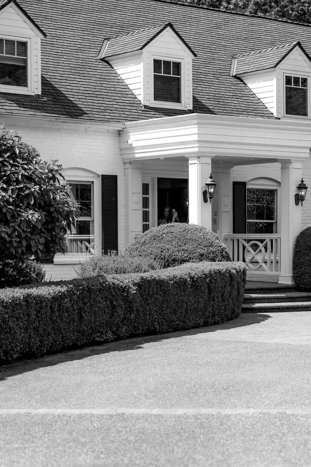 Elegant white colonial style house exterior with manicured hedges and gravel driveway showcases classic architectural details.