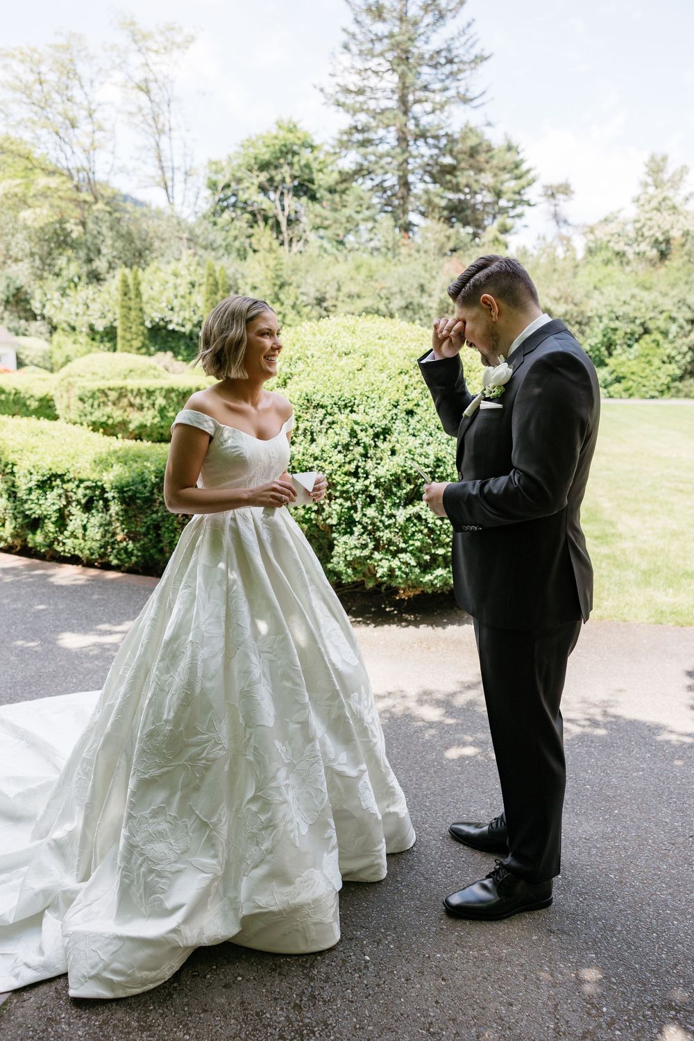 A couple shares a romantic first look moment in an outdoor garden setting, with the bride in a stunning white ballgown.