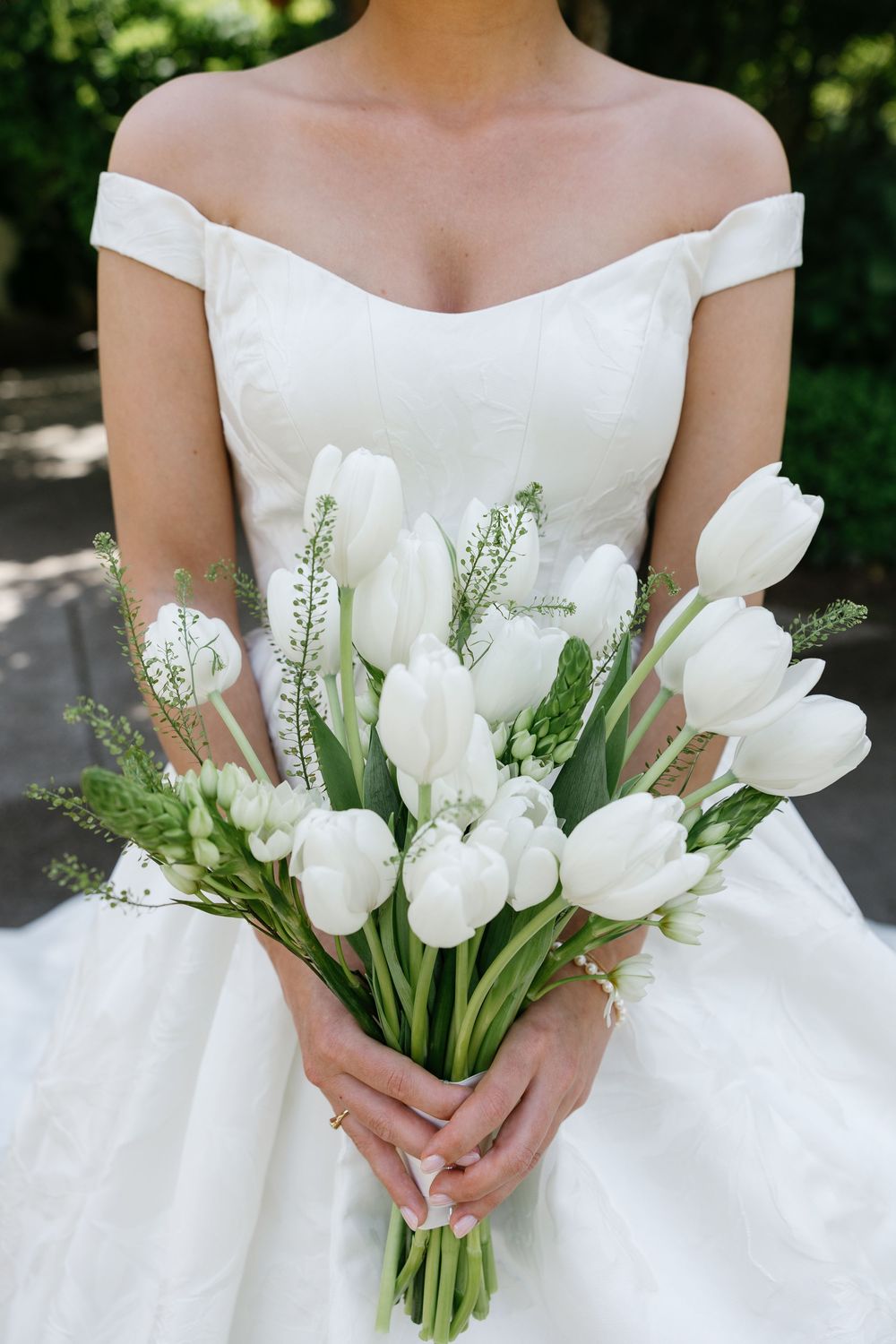 A classic white tulip and greenery bridal bouquet held against an elegant wedding dress.