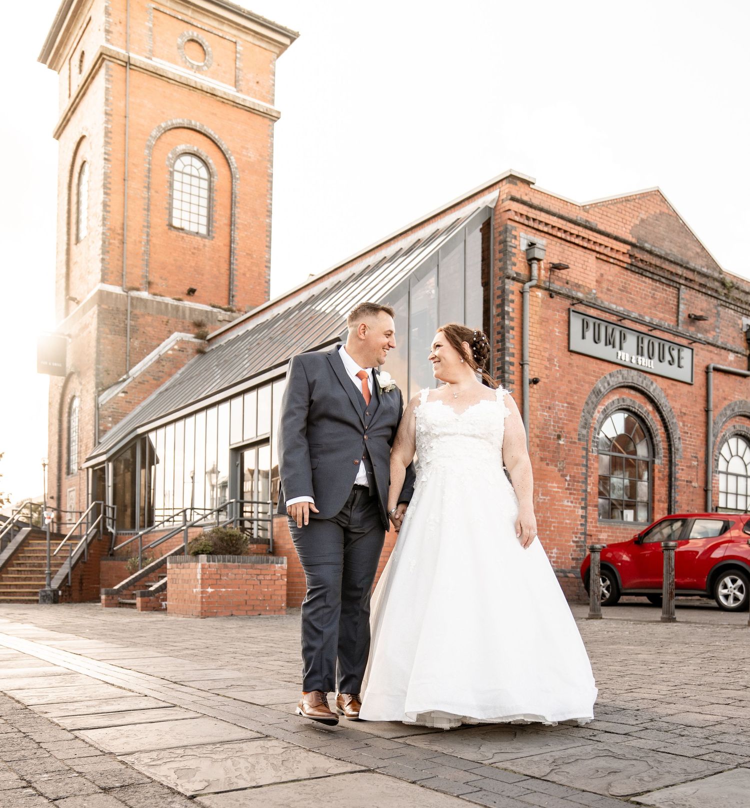 A couple in formal wedding attire walking up historic brick stairs with curved railings and red brick building wall.