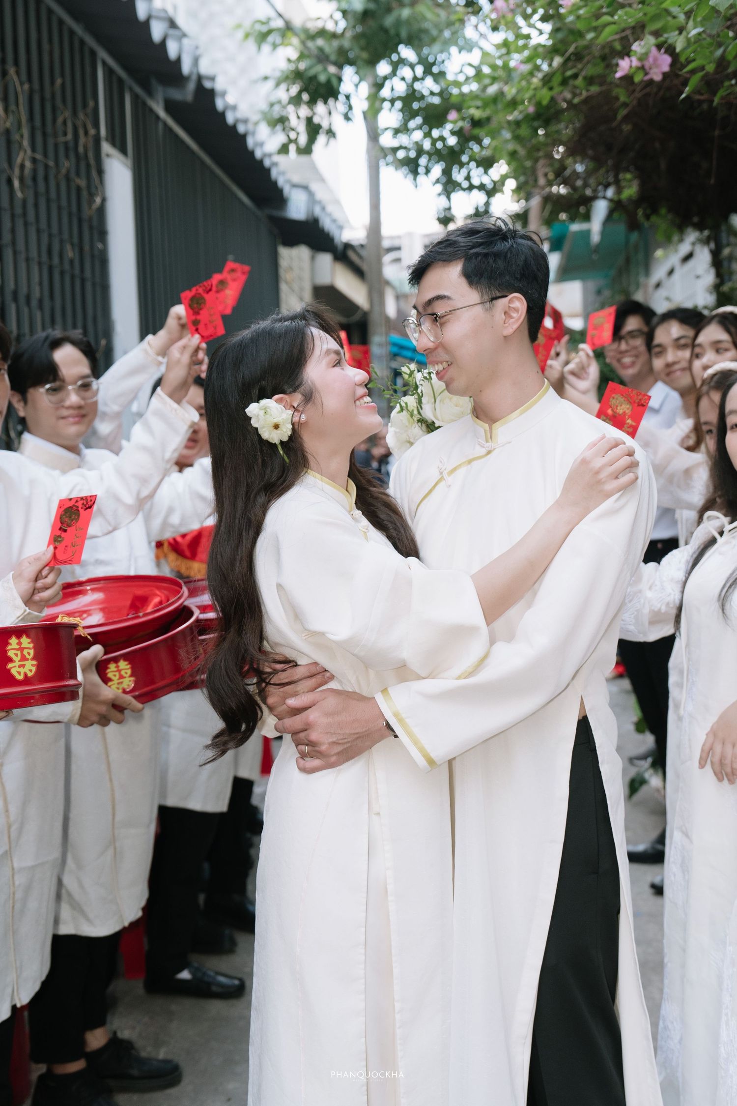 Smiling Vietnamese bride and groom embrace lovingly during outdoor traditional wedding procession.
