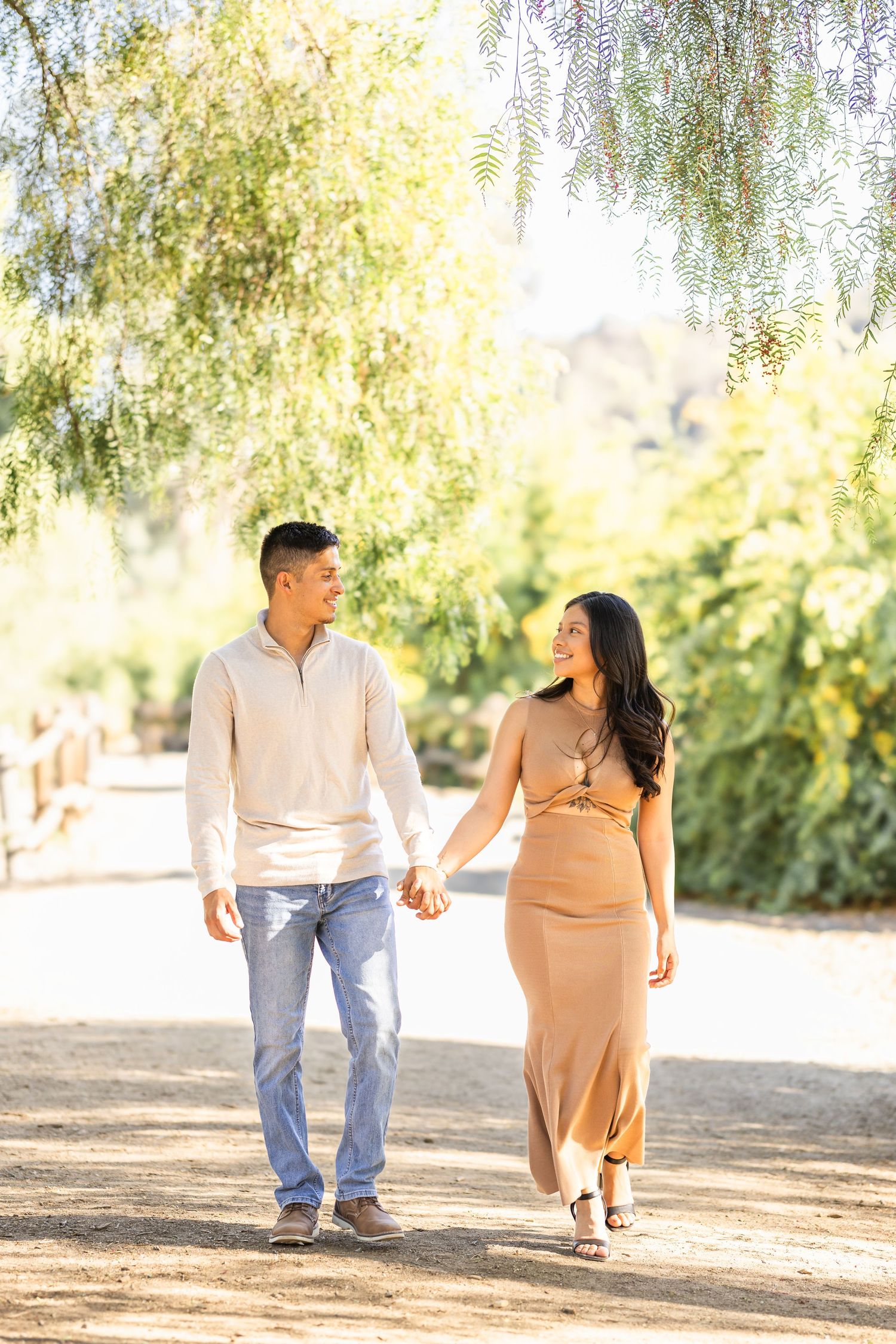 Couple walking together on a sunlit path under weeping willow trees.