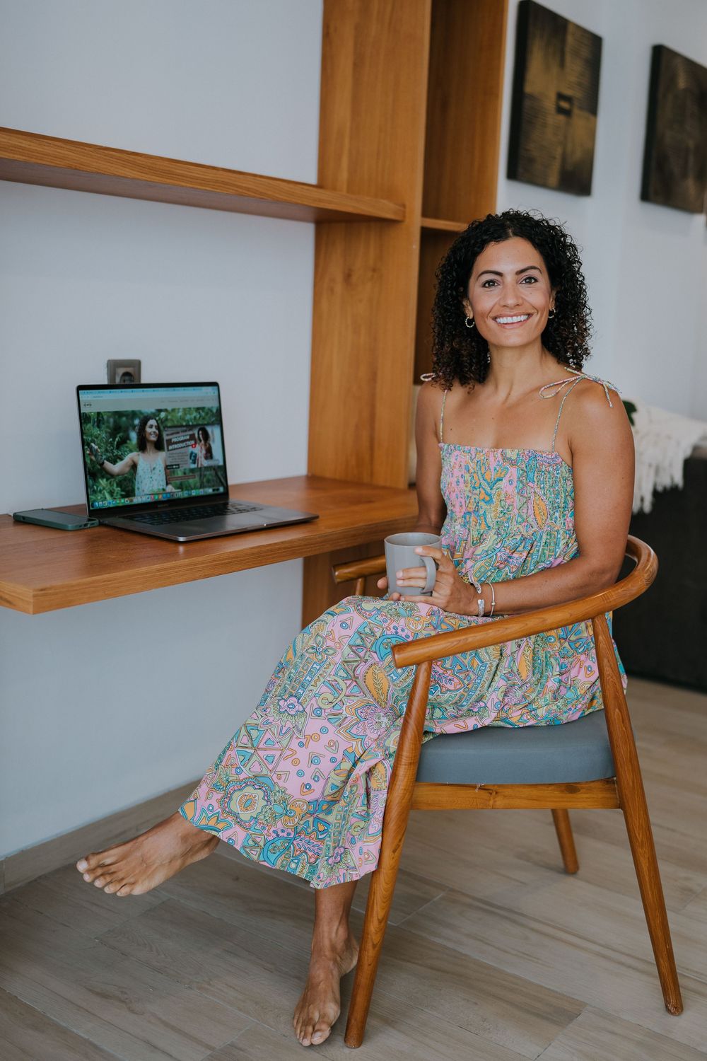 Someone relaxes in a floral dress on a wooden chair in a modern interior setting.