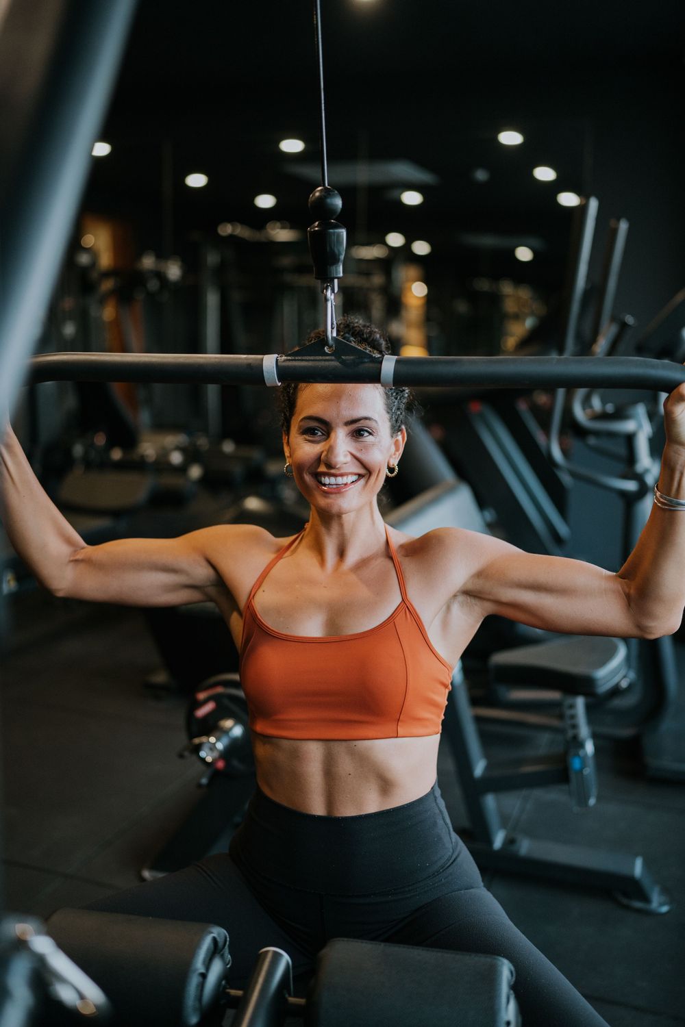 Athletic workout session at gym showing lat pulldown exercise in orange sports bra.