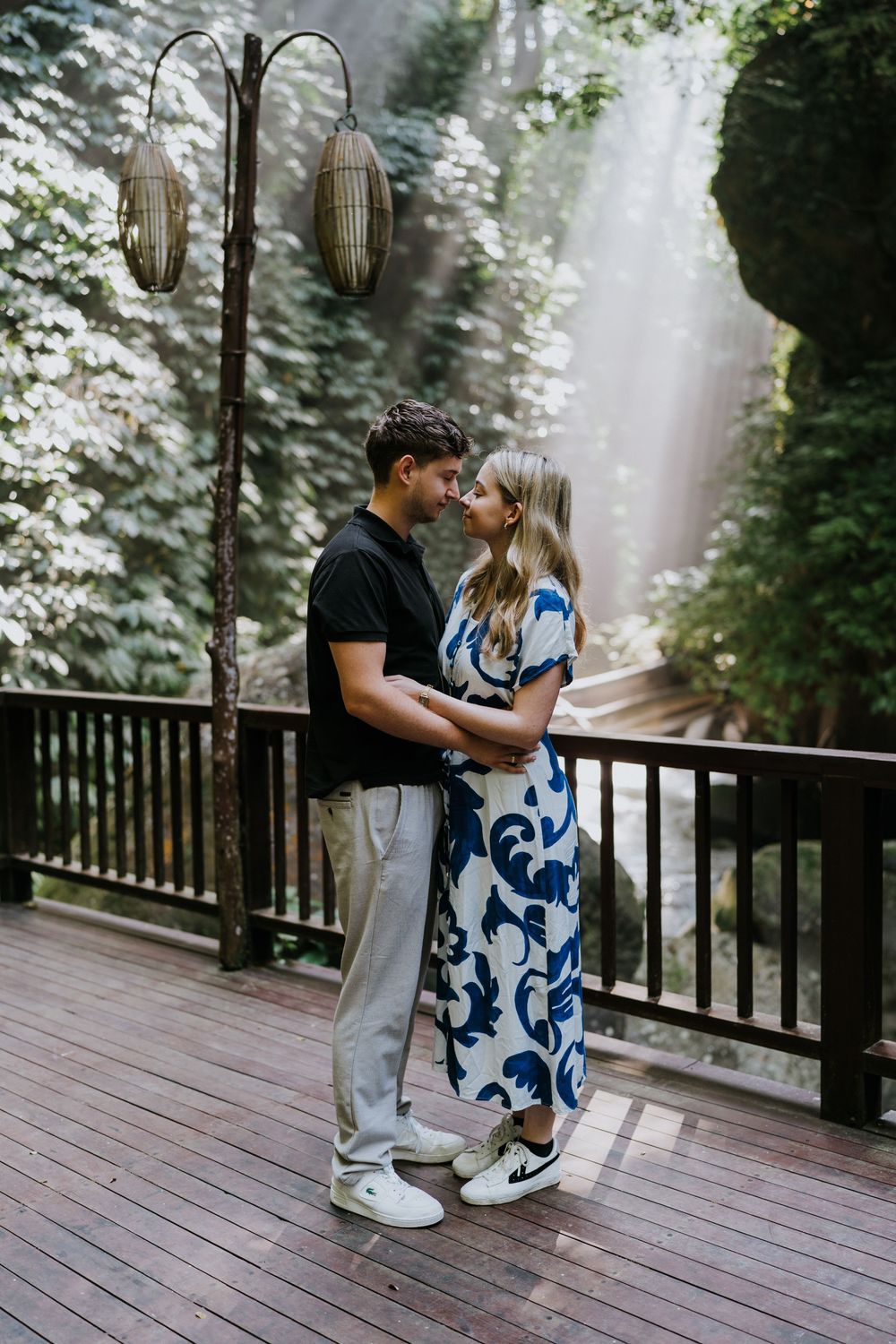 A romantic couple embraces on a wooden deck surrounded by misty forest and decorative lanterns.