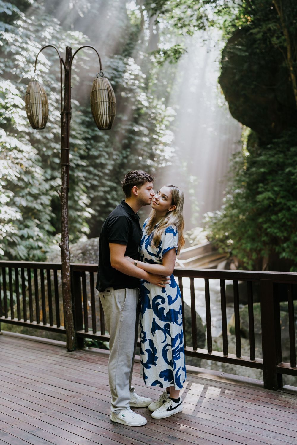 A couple shares an intimate moment on a wooden deck with hanging lanterns and misty forest views.
