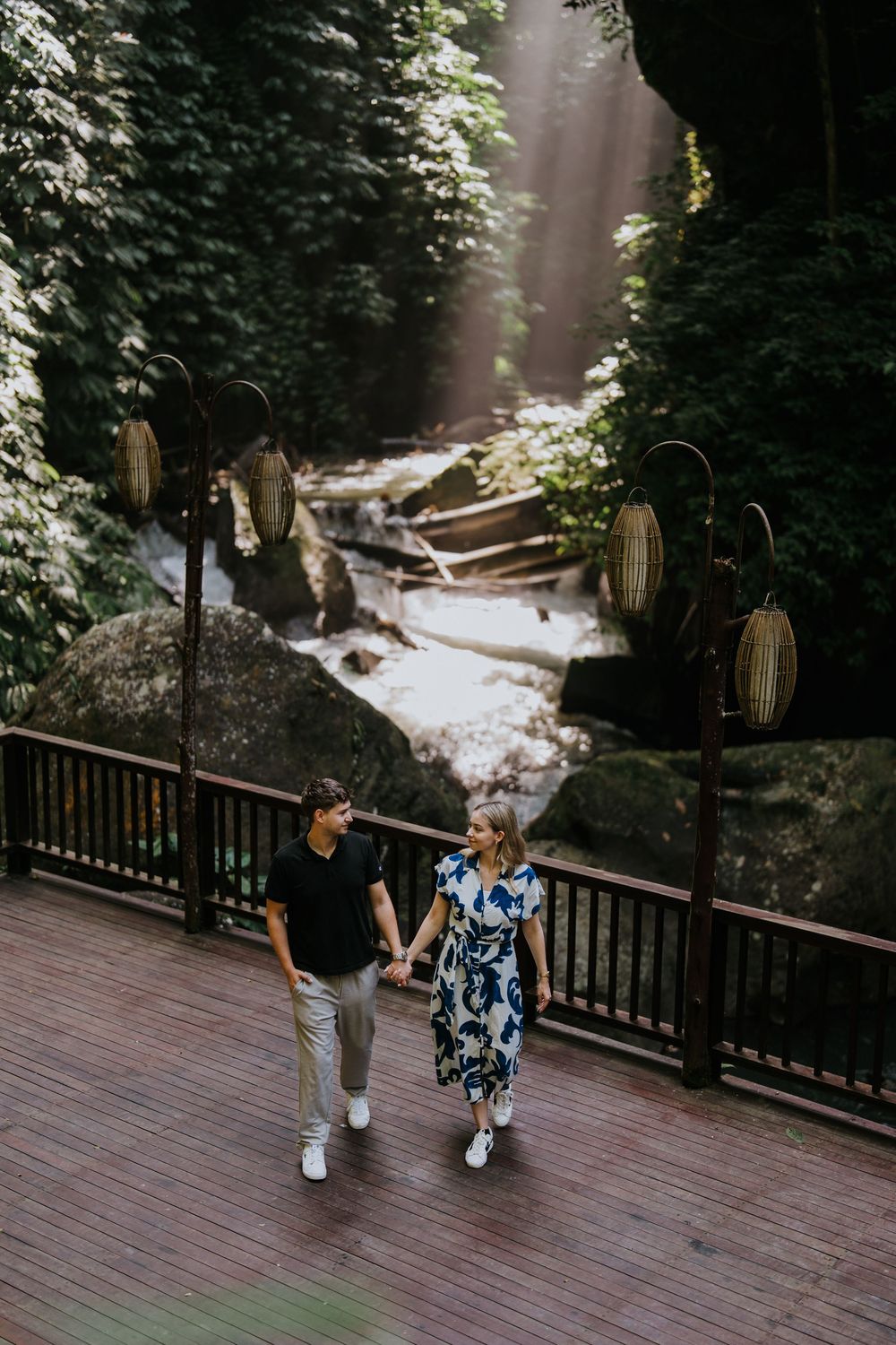 Couple walking together on a wooden deck surrounded by lush forest scenery.
