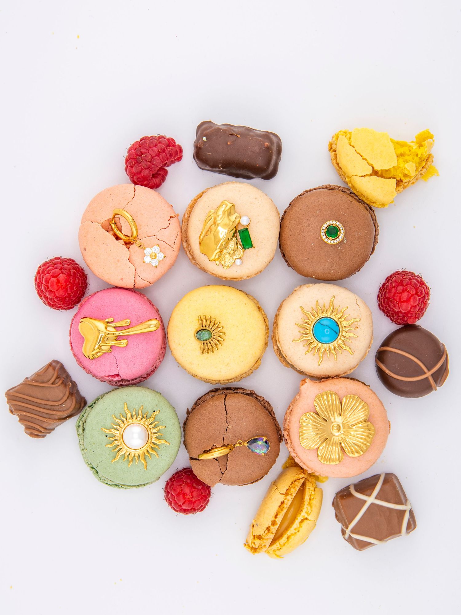 Colorful macarons with floral designs and raspberry accents arranged on white background.