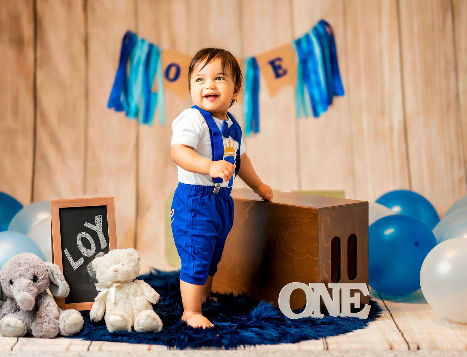 Birthday celebration setup with blue decorations, white balloons, and stuffed animals for a one year milestone photo session.