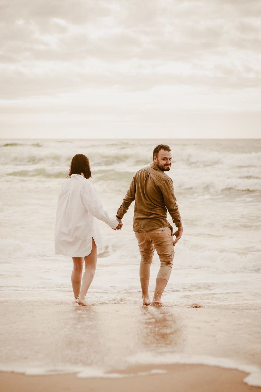 Couple marchant pieds nus ensemble le long du rivage de l'océan au coucher du soleil.