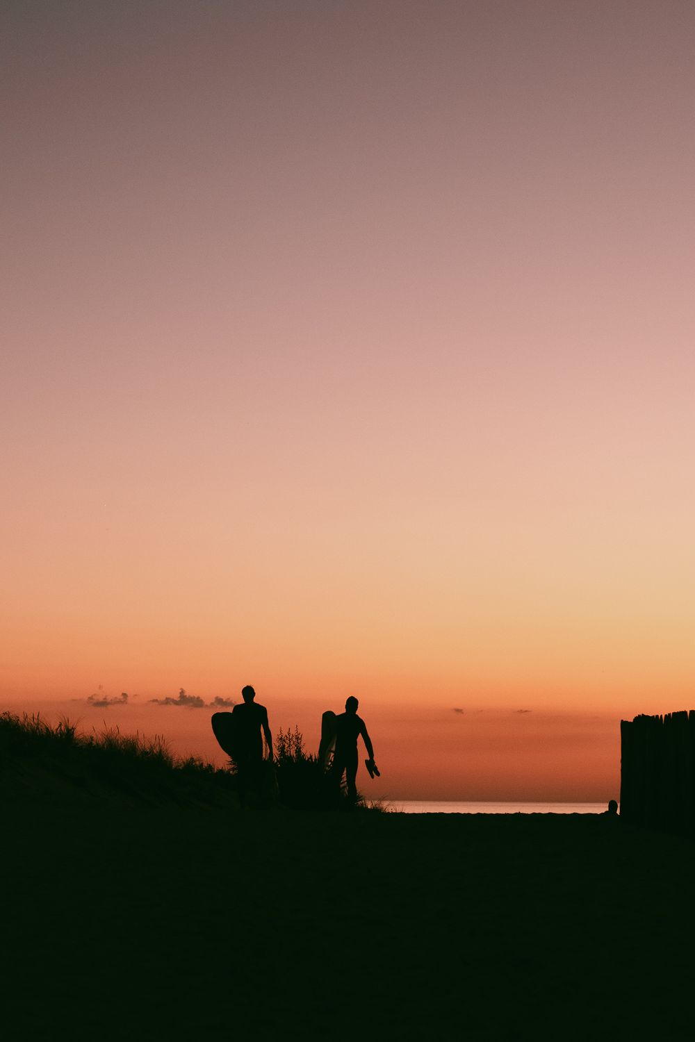 Deux silhouettes se tiennent sur une colline contre un ciel de coucher de soleil orange et rose vibrant.