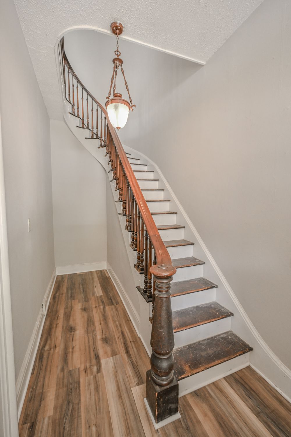 Elegant curved staircase with white risers, dark wood treads, and vintage-style pendant light in renovated home interior.