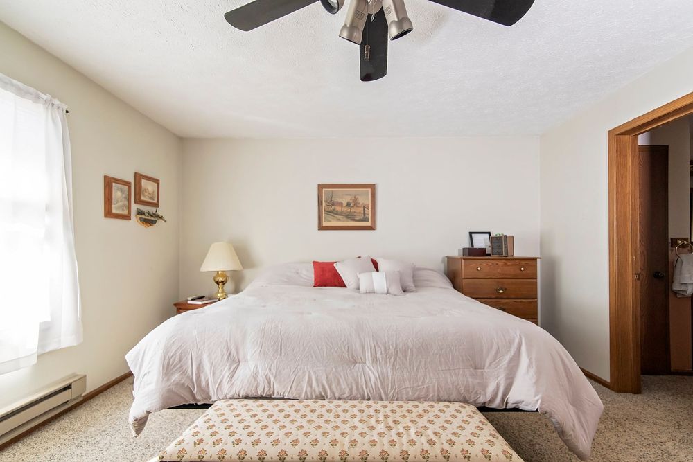 Bright master bedroom with wooden floors, white linens, and large windows for natural light.
