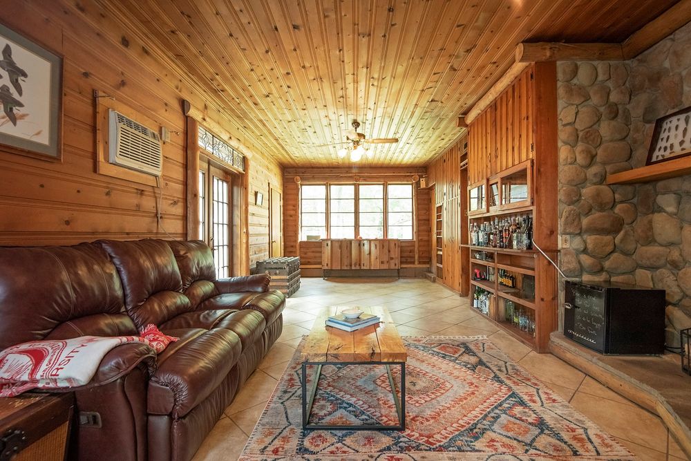Rustic living room with wood-paneled ceiling, stone fireplace, and leather furniture.