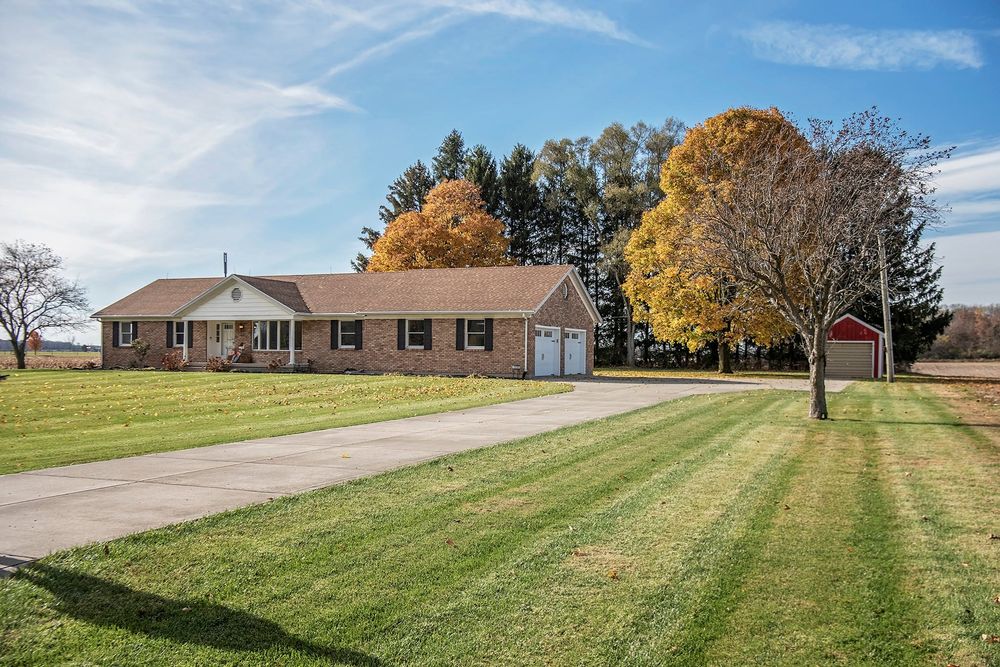 Scenic rural property with fall trees and expansive green lawn under blue sky.