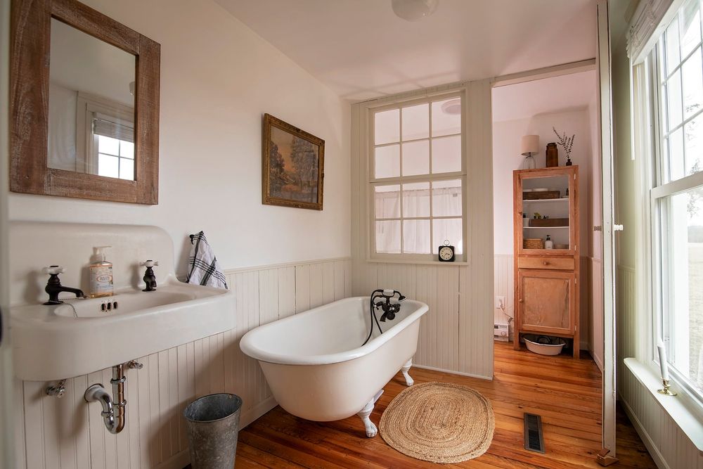 Modern bathroom featuring white clawfoot tub, exposed wooden beams, and vintage fixtures against white walls.