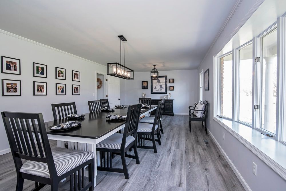 Long dining room with black chairs, white walls, and large windows providing natural light.