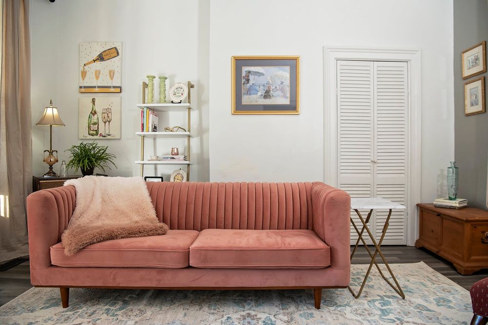 Living room featuring a long salmon-colored sofa, framed artwork, and white walls.