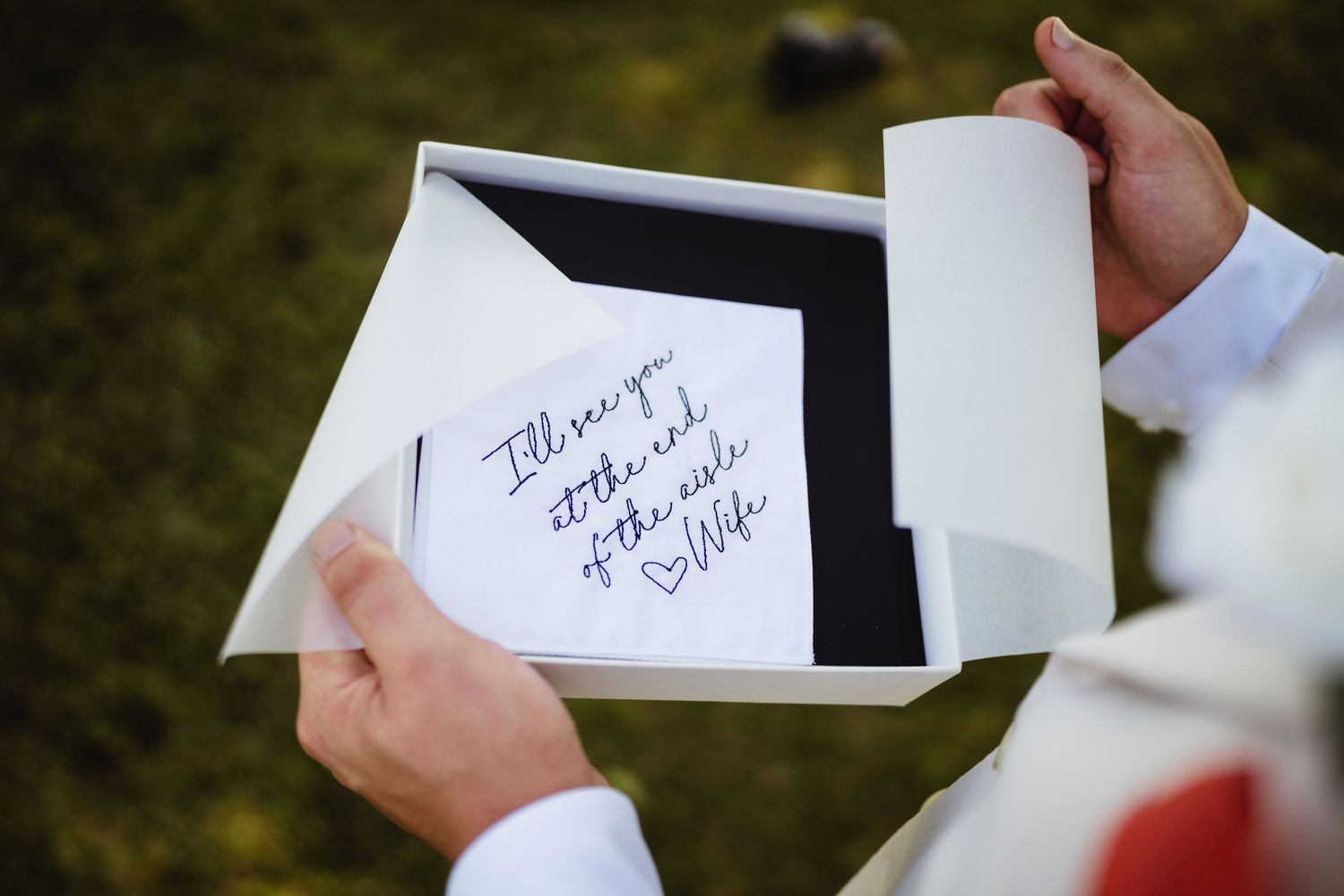 Someone wearing a red jacket writes on small white pieces of paper in an outdoor setting.