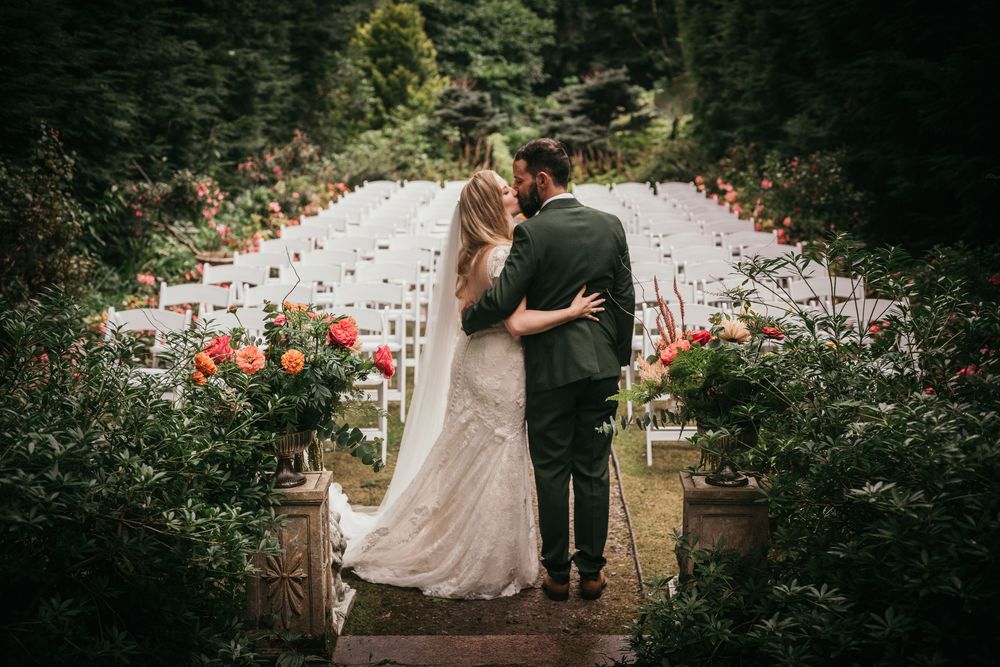Bride and groom embracing while overlooking an outdoor wedding ceremony in a rose garden.