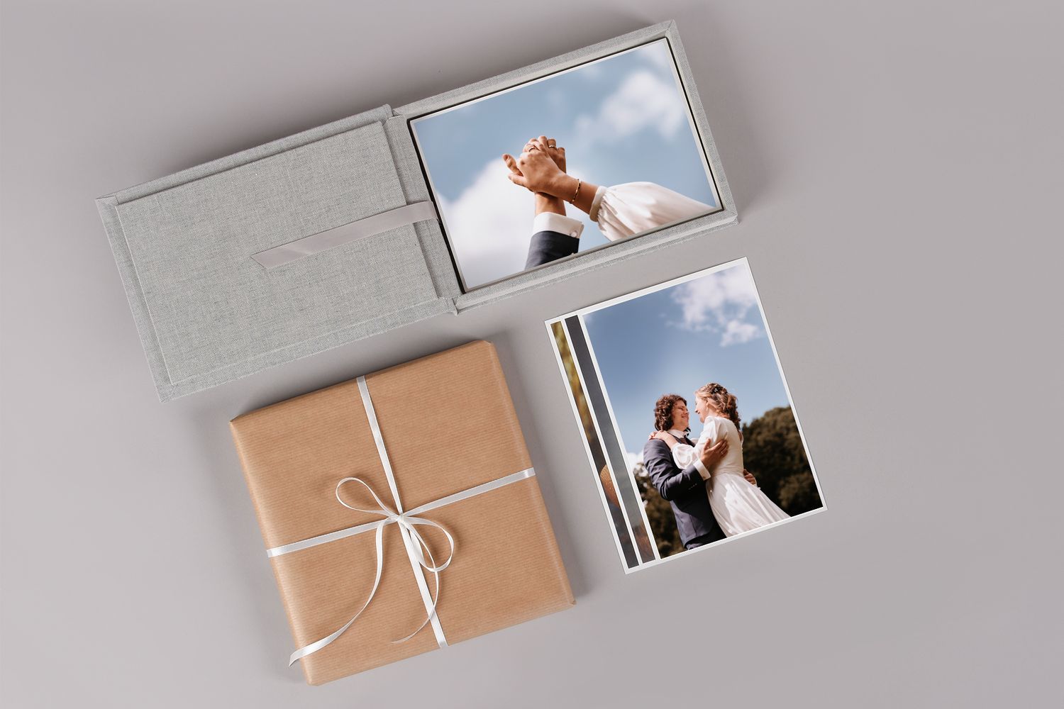 Minimalist wedding photo album and gift box with ribbon arranged on light gray background.