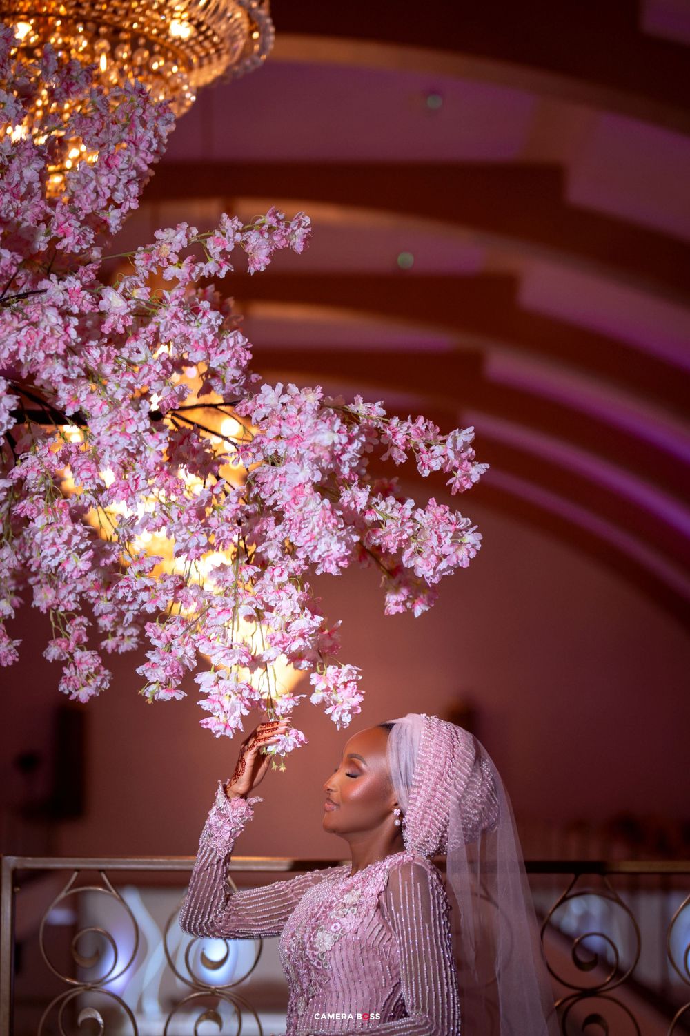 Elegant floral arrangement featuring delicate pink cherry blossoms illuminated by warm lighting in an indoor venue.