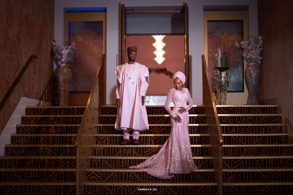 Two people in elegant pink attire pose on grand staircase in matching outfits for formal evening occasion.