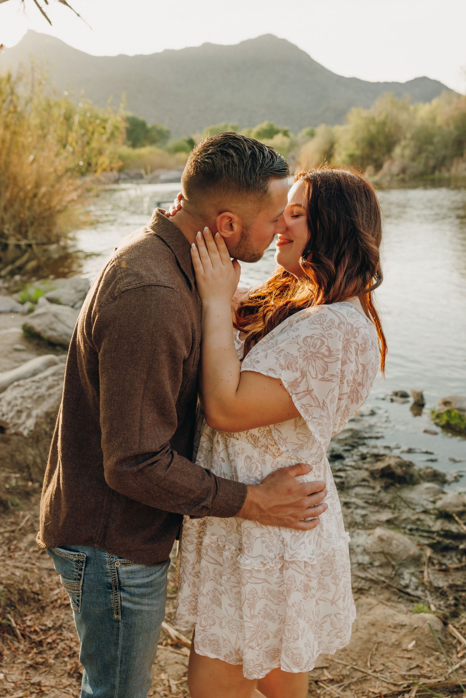 Romantic couple embraces by the scenic Salt River during golden hour in a desert mountain landscape.