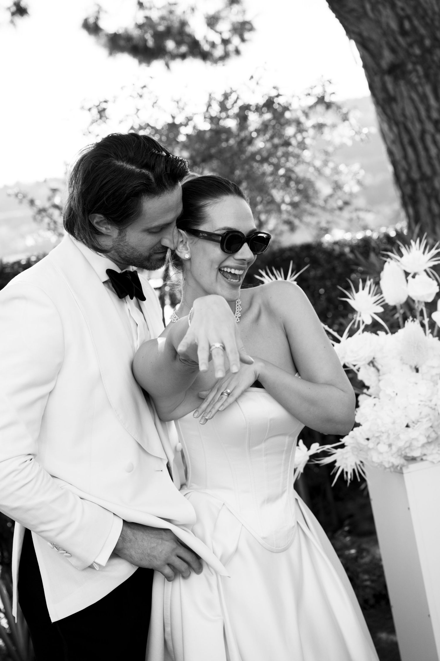 A couple dancing together under elegant stone archways with palm trees visible in the background.