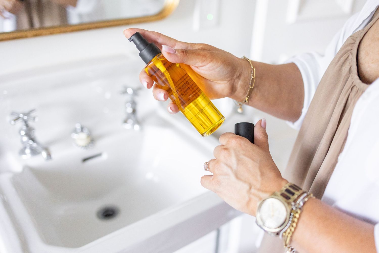 close up of woman wearing linen dress and button up shirt applying Lovefresh body oil to hands
