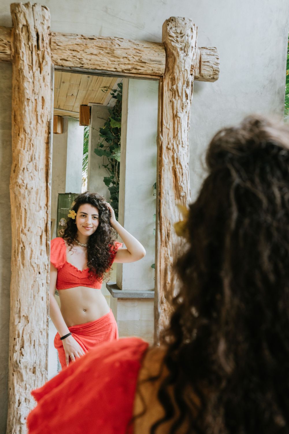 Figure in red dress posing gracefully against rustic wooden pillars in an outdoor setting.