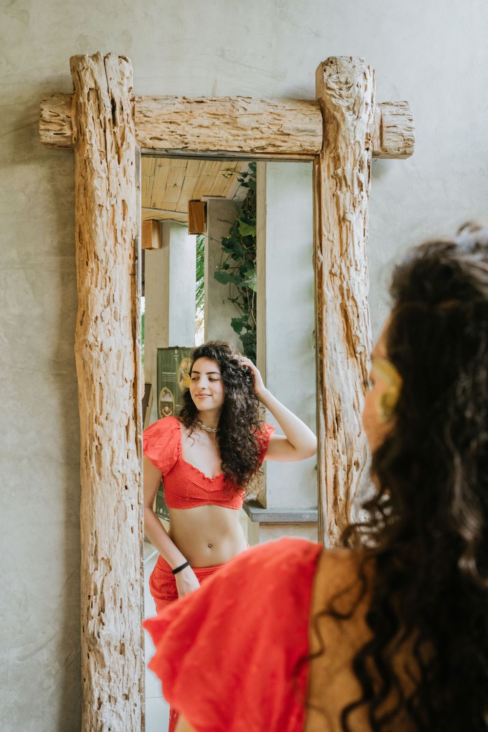 Figure in red outfit looking in mirror framed by rustic wooden posts.