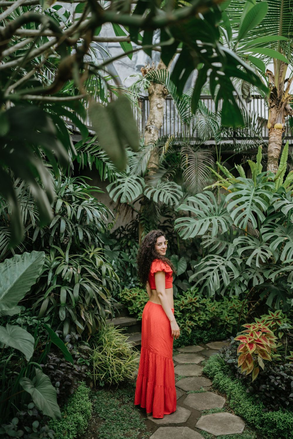 A winding garden path leads through lush tropical plants and monstera leaves.