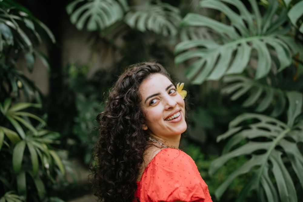Person in coral dress poses playfully against tropical foliage backdrop.