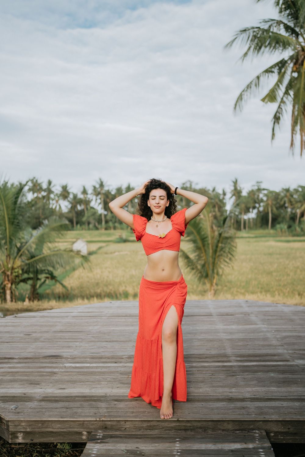 A red dress photoshoot on a wooden deck overlooking palm trees and rice fields.