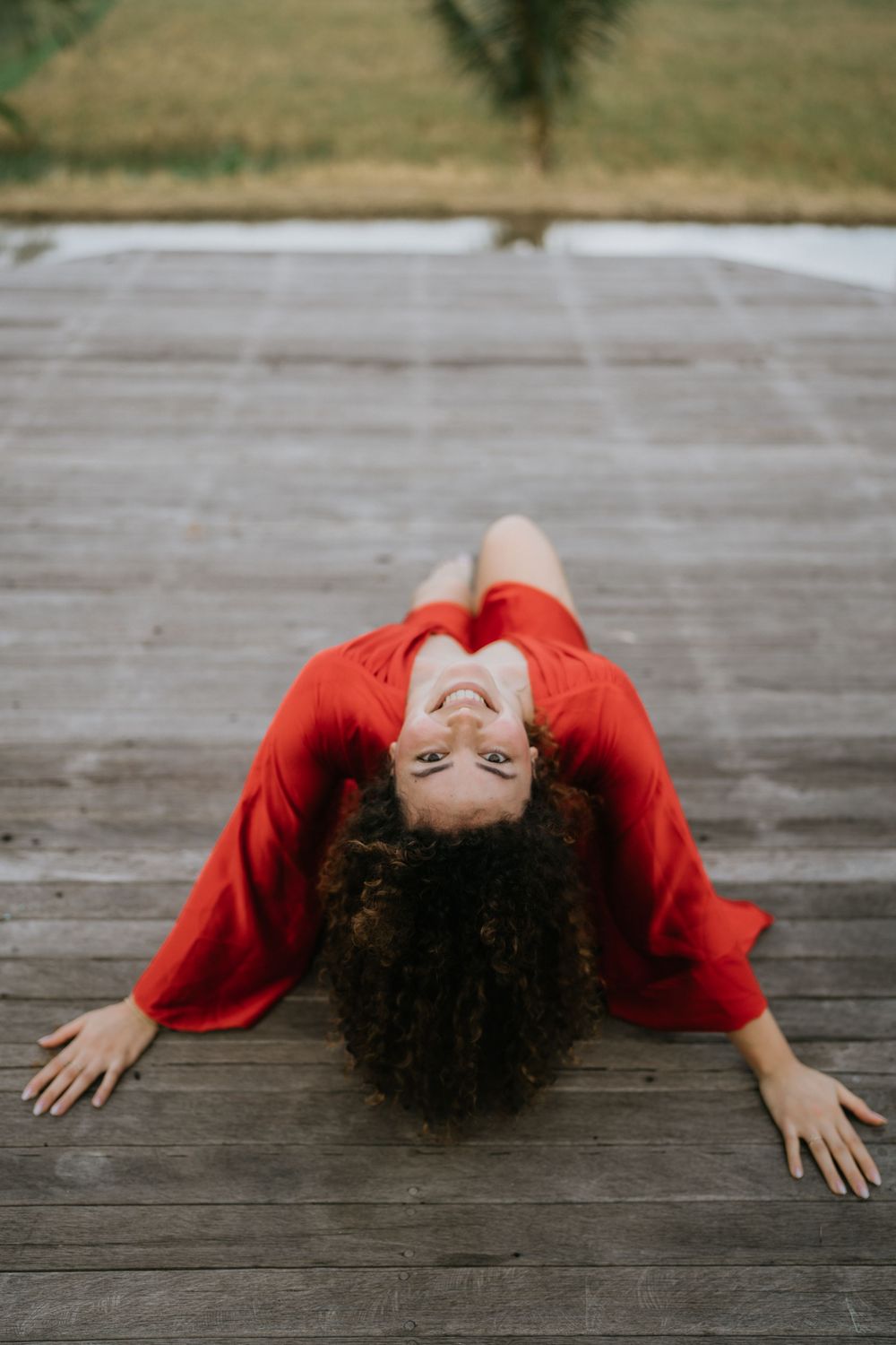 A dramatic pose in a flowing red dress on a wooden deck outdoors.
