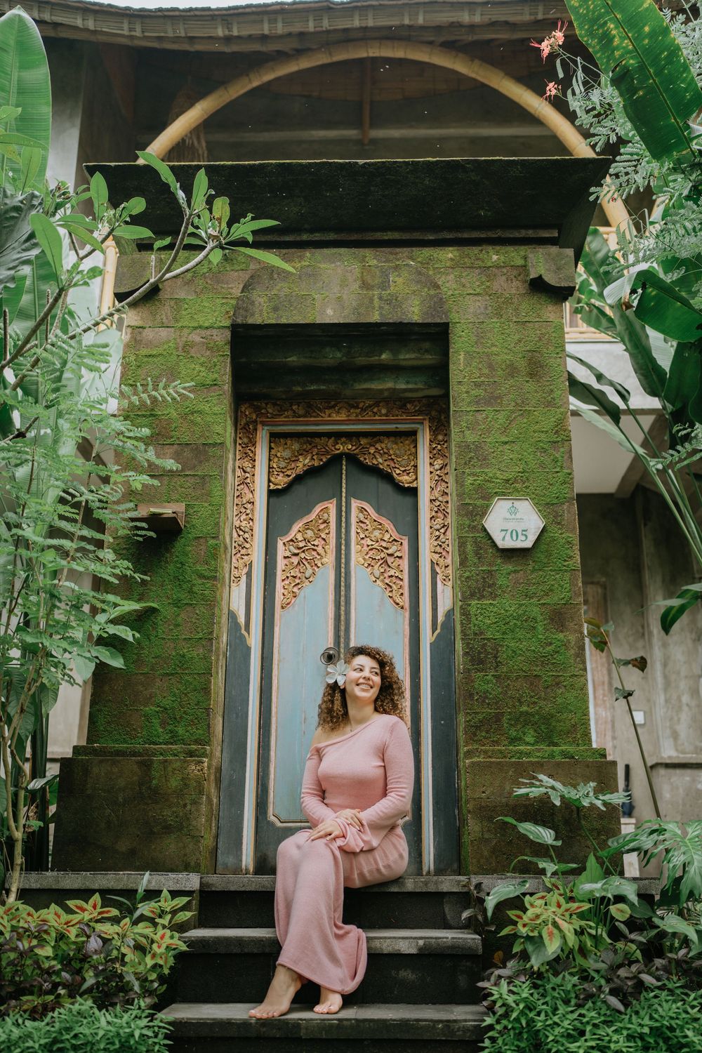 A pink dress photoshoot in a lush tropical garden setting with ornate architectural details.