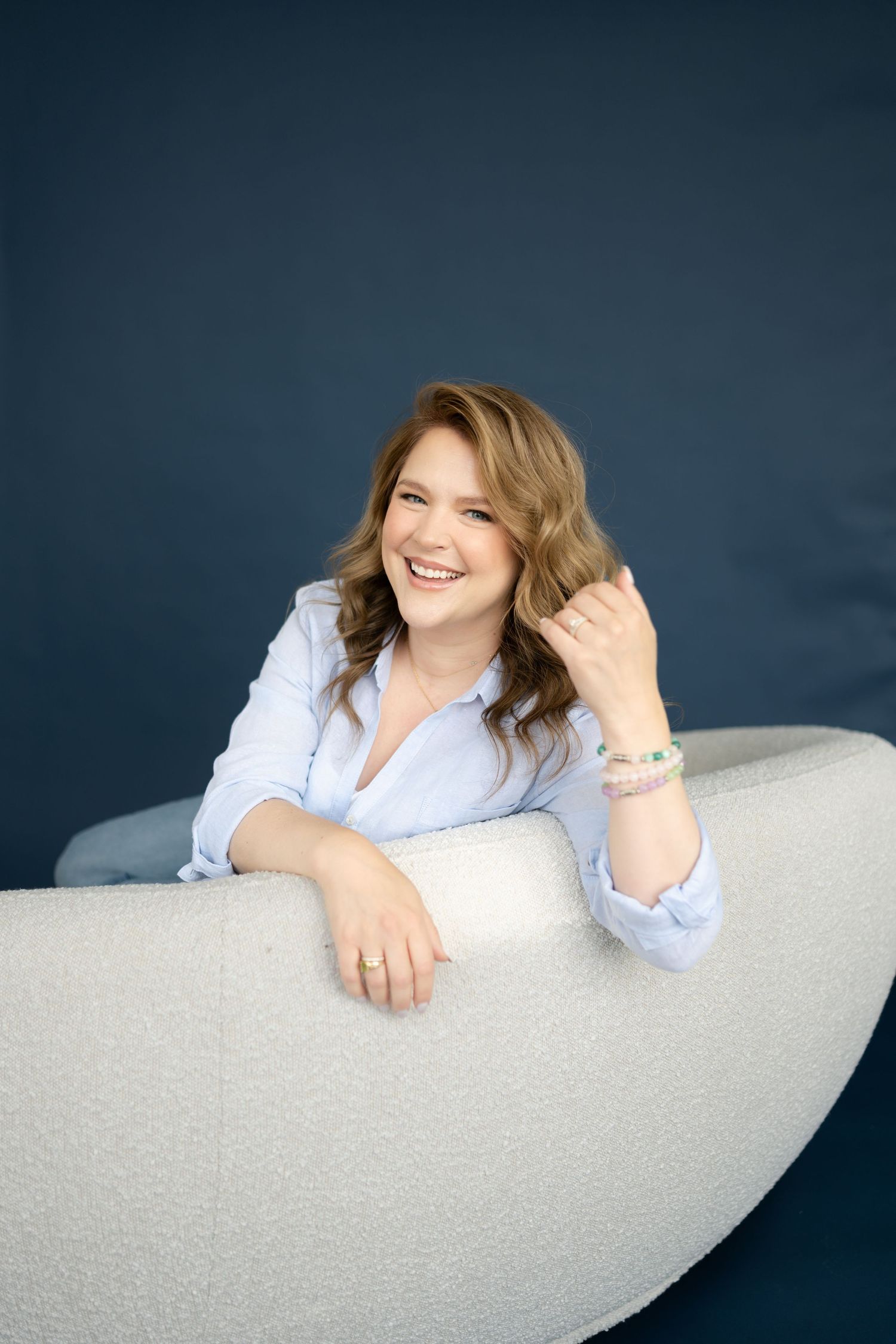 Woman rests on curved white sofa against dark navy wall in studio setting.