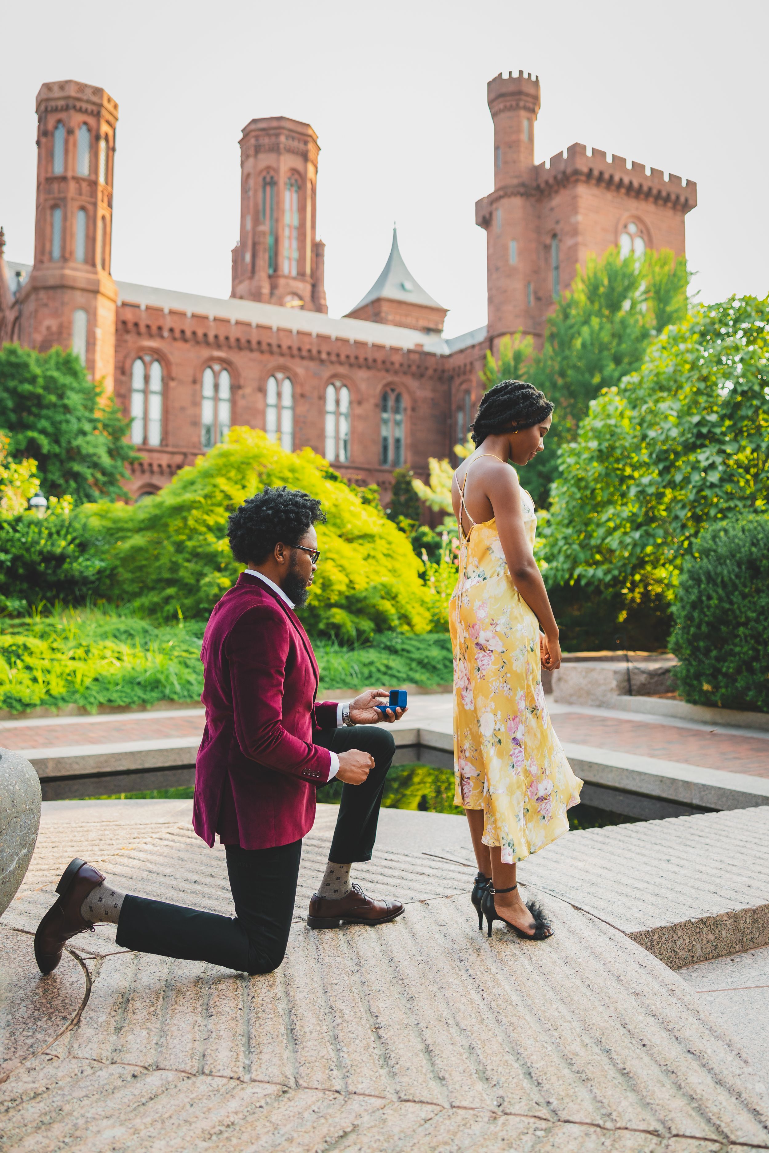 A romantic marriage proposal sequence taking place on stone steps outside a historic castle-like building with red brick walls.
