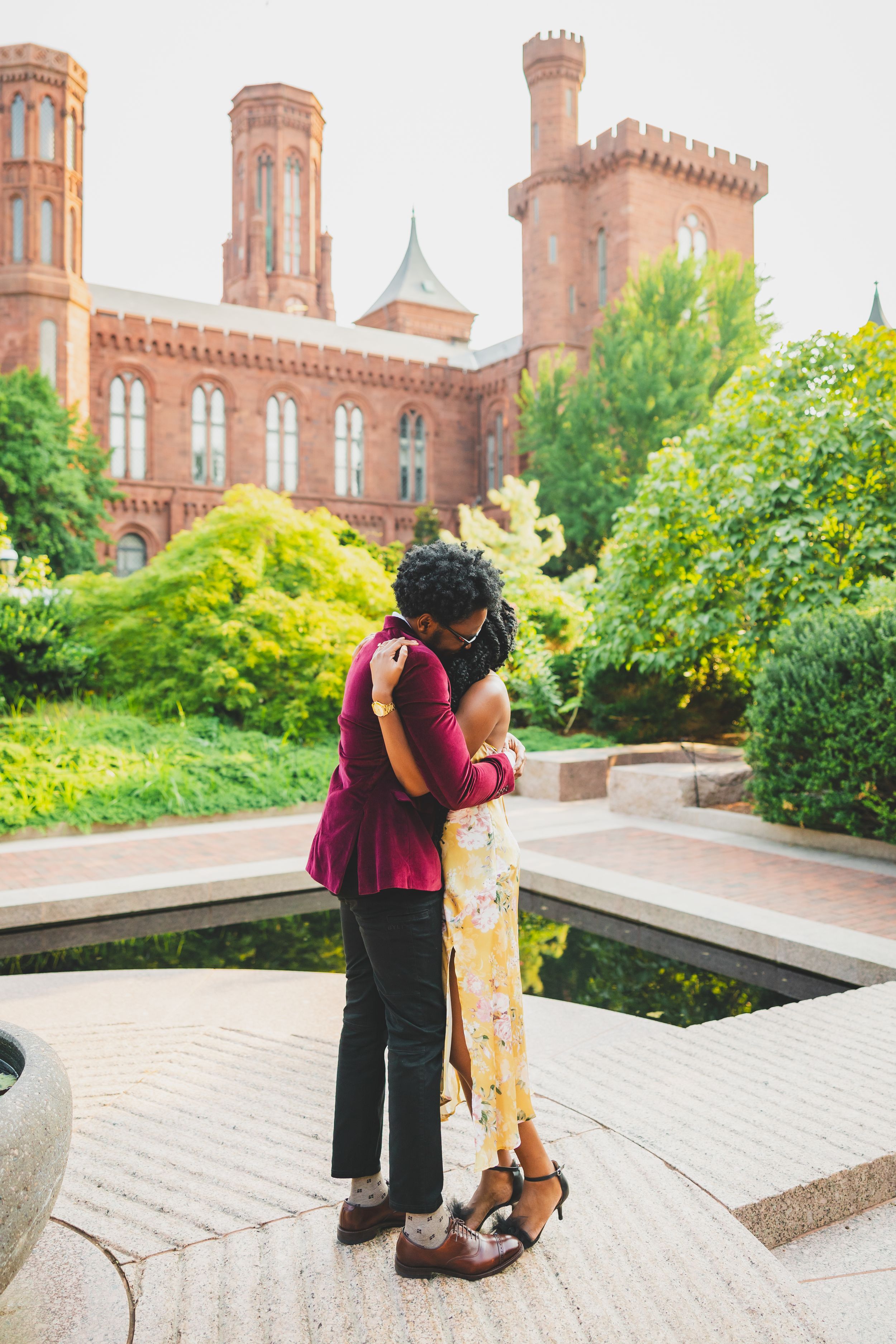 A romantic couple embraces in front of the historic Smithsonian Castle building on a sunny summer day.