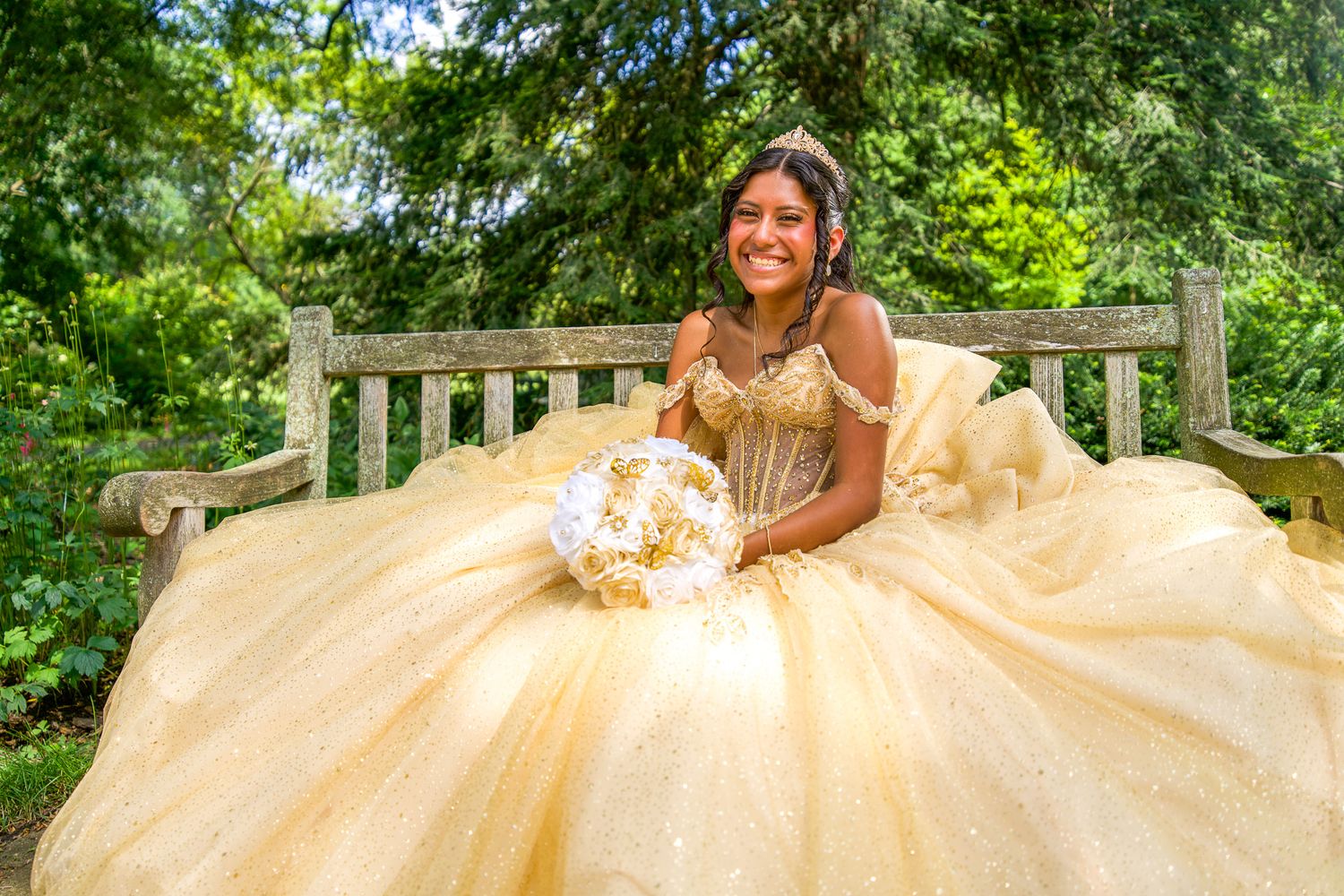QUINCEAÑERA Elegant gold ballgown dress photographed in a lush garden setting with natural lighting.