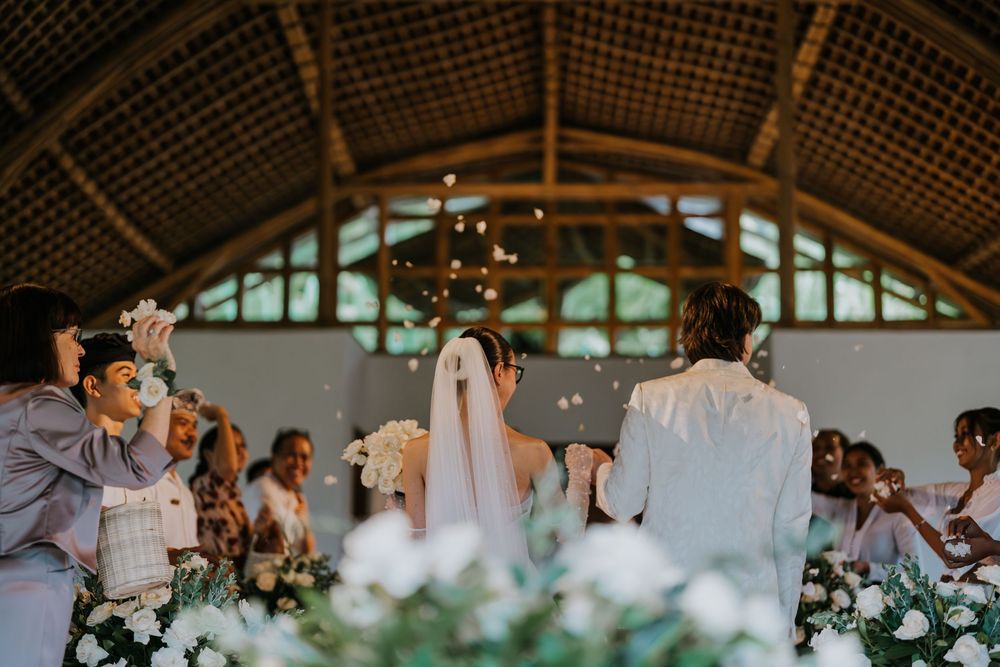 Wedding reception scene under a rustic wooden pavilion with decorative lighting and floral arrangements.
