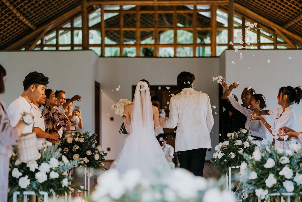 Wedding guests celebrate during a reception in a rustic wooden barn venue with elegant floral decorations.