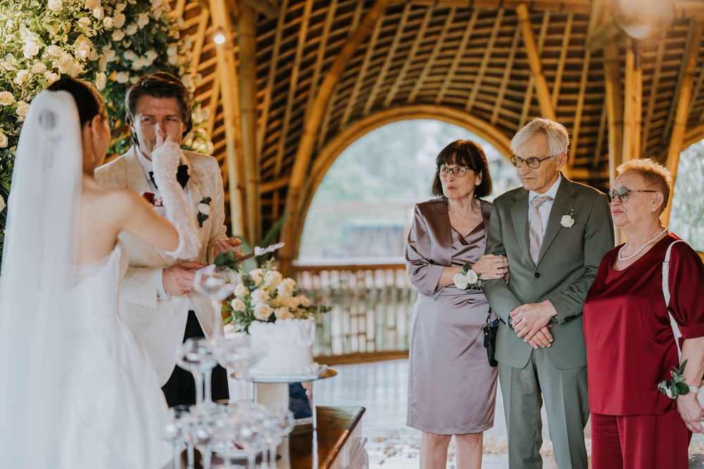 Wedding party gathers for group photos in a rustic barn setting with white floral arrangements.